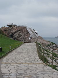 Footpath leading towards sea against sky