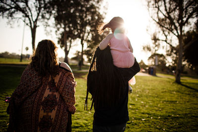 Niece on uncle's shoulders walking with aunt and sunset