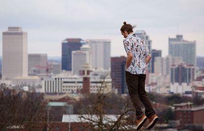 Rear view of man jumping against buildings in city