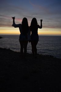 Silhouette friends standing on beach against sky during sunset