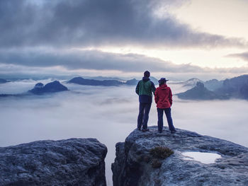 Rear view of men standing on rock against sky during winter