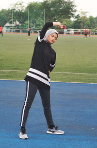 Full length of athlete wearing hijab while exercising on playing field