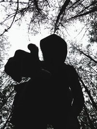 Rear view of silhouette man and woman standing by tree against sky