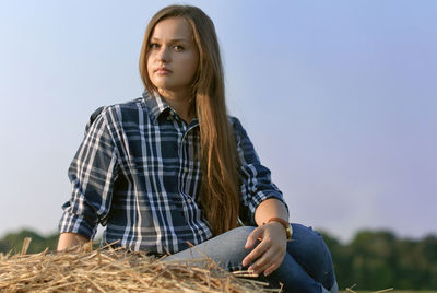 Portrait of confident beautiful woman sitting on straw against sky