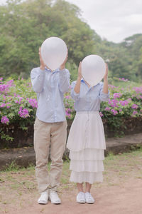 Couple holding balloons while standing on field against trees in park
