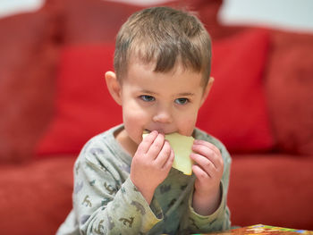 Cute young boy eating cheese at home while watching tv next to the couch