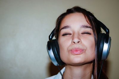 Close-up of woman with eyes closed wearing headphones while puckering against wall