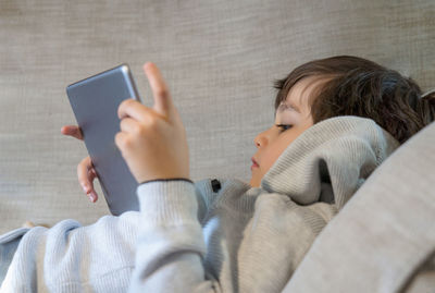 Cute boy using digital tablet while lying on sofa at home