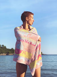 Woman wrapped in a towel while standing in sea against sky