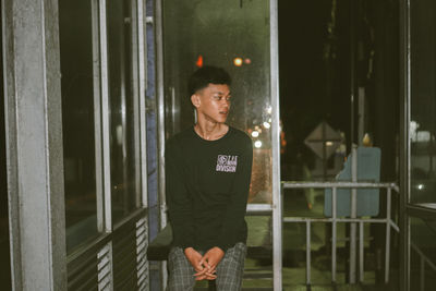 Young man looking away while standing against glass