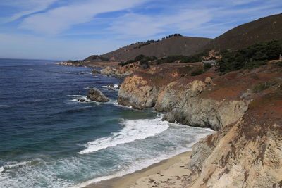 Scenic view of seascape by mountain against blue sky