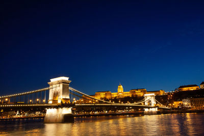 Illuminated bridge over river against blue sky