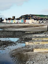 Reflection of building in puddle on beach against sky in city