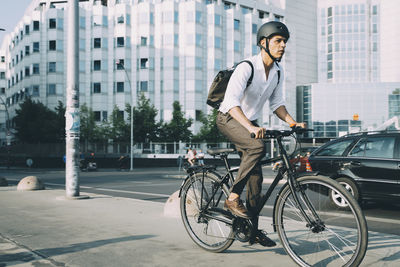 Full length of businessman riding bicycle on sidewalk against building in city