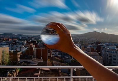 Close-up of hand holding glass against buildings in city