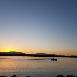 Silhouette man sailing boat on lake against sky during sunset