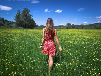 Rear view of woman in colorful dress standing on a field with green grass and yellow flowers