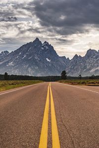 Empty road leading towards mountains against sky