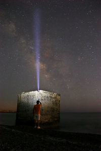 Rear view of man standing by sea against sky at night