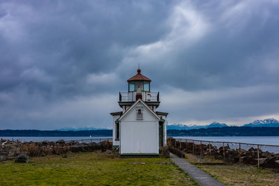 Lighthouse amidst sea and buildings against sky