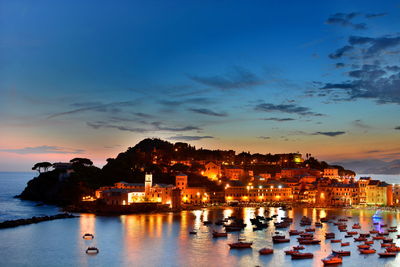 High angle view of boats moored on sea against illuminated buildings at sunset