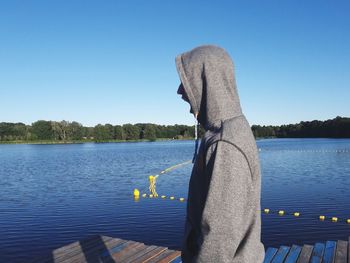 Man on pier over lake against clear blue sky