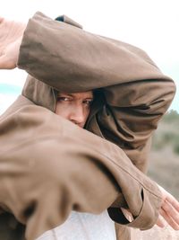 A man in a brown raincoat covers his face with his hands