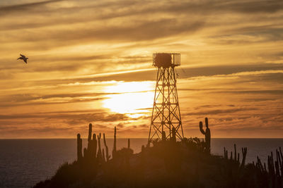 Silhouette tower by sea against sky during sunset