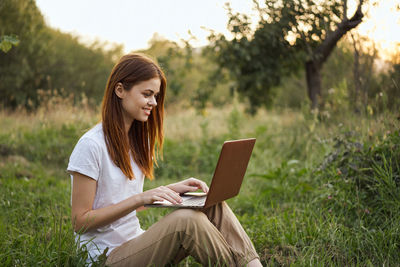 Young woman using digital tablet while sitting on field