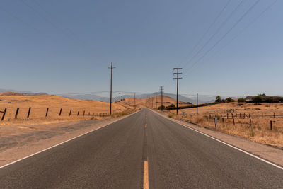 Road by electricity pylons against sky