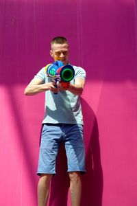 Man shooting with toy handgun while standing against pink wall