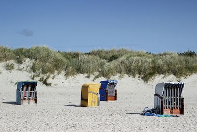 Hooded chairs on beach against clear sky