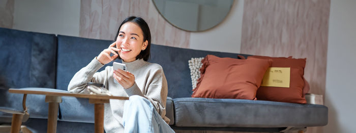 Young woman using mobile phone while sitting on sofa at home