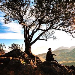 Man sitting on rock against sky