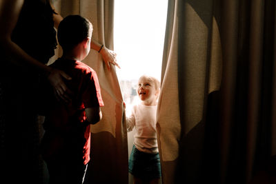 Girl standing by window looking at mother with boy in hotel room