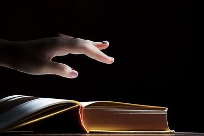 Close-up of hand holding book against black background