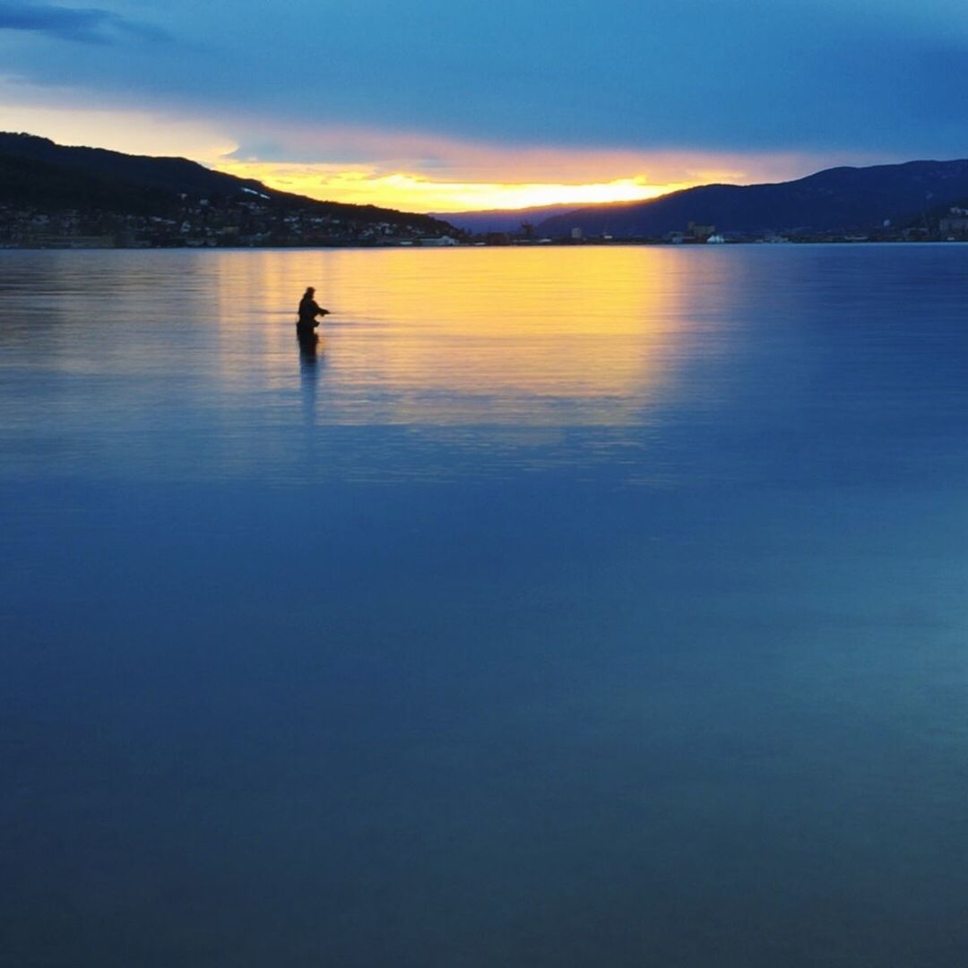 water, mountain, tranquil scene, silhouette, scenics, tranquility, beauty in nature, sunset, sky, lake, nature, mountain range, reflection, idyllic, sea, one person, outdoors, rippled, one animal, calm