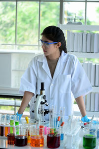 Woman standing by chemicals in glassware at laboratory