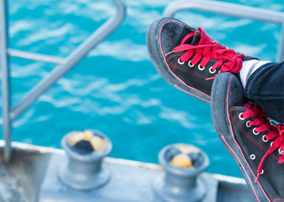 Close-up of person wearing black canvas shoes against blue sea at harbor