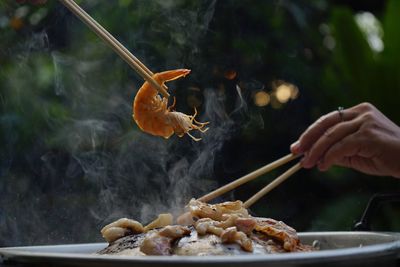 Person holding meat on barbecue grill