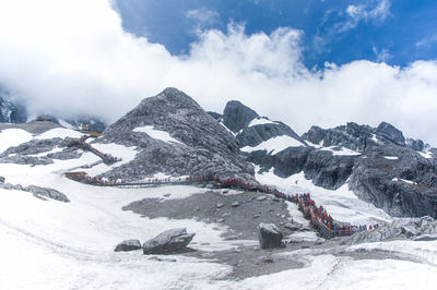 Low angle view of jade dragon snow mountains against cloudy sky on sunny day