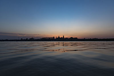 Silhouette of city at riverbank during sunset