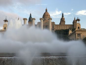 Fountain with mist  in front of building against sky in barcelona 
