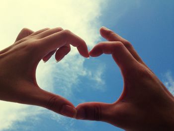 Low angle view of human hands making heart shape against sky