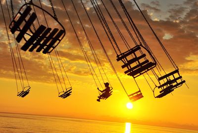 Low angle view of silhouette boy riding over sea against sky during sunset