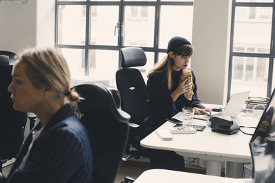 Businesswoman eating food while working on laptop at office