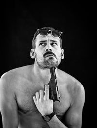 Shirtless man attempting suicide with gun against black background