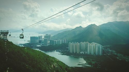 Overhead cable car against buildings and mountains against cloudy sky at ngong ping 360