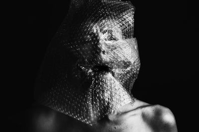 Close-up of shirtless boy with bubble wrap against black background