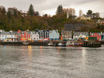 Boats in river by buildings against sky